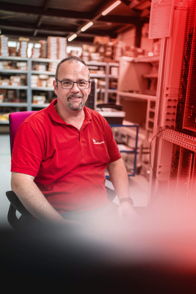 Ein Mann in rotem Arbeits-Shirt lächelt in die Kamera