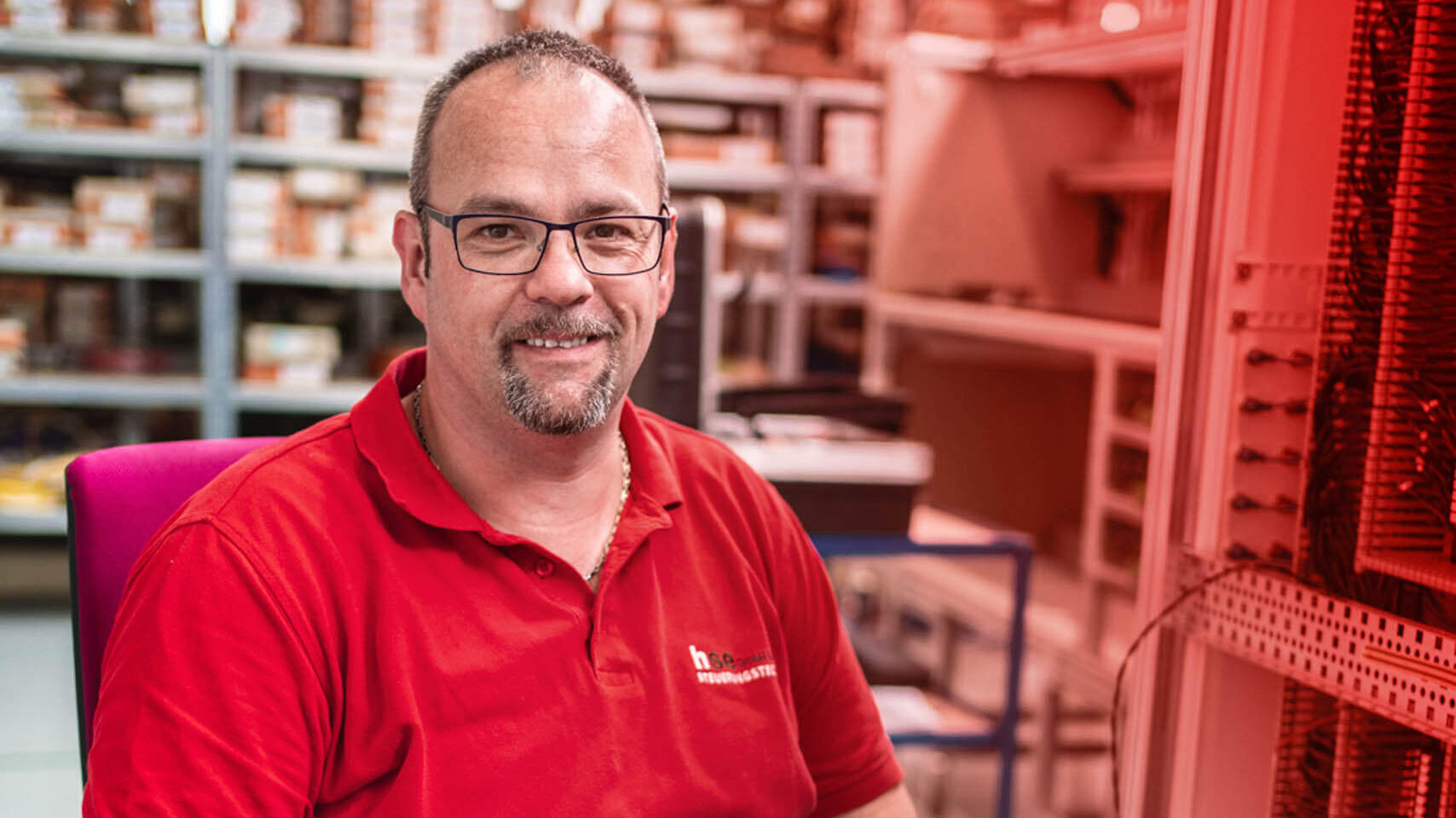 Ein Mann in rotem Arbeits-Shirt lächelt in die Kamera